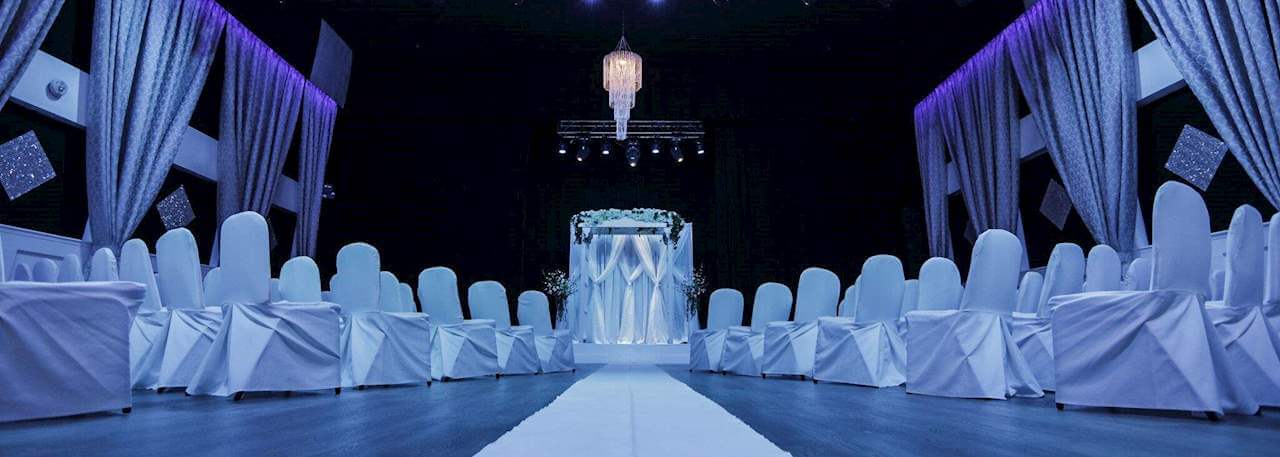 A decorated meeting room with white chairs, curtains, and an aisle leading to an archway.