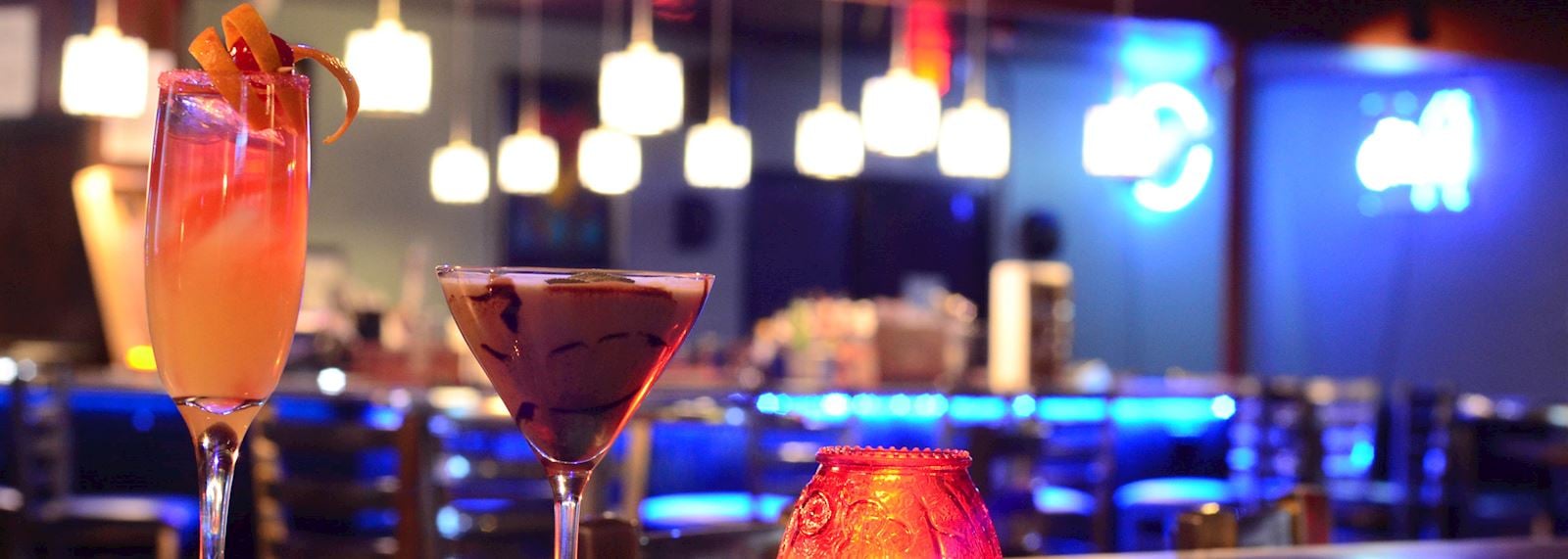 Two cocktails on a bar with a neon sign in the background.