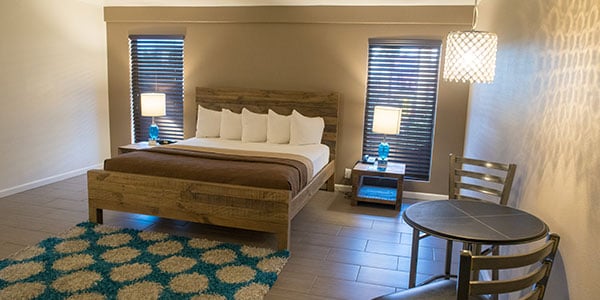 A wide view of a hotel room with a bed, table, chair, and rug.