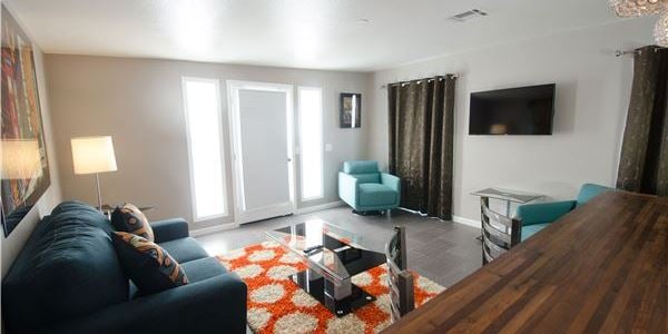 A wide-angle view of a hotel suite's living area with a sofa, coffee table, TV, and dining table.