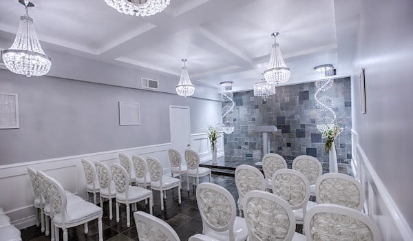 A wedding chapel with white chairs, chandeliers, and gray walls.